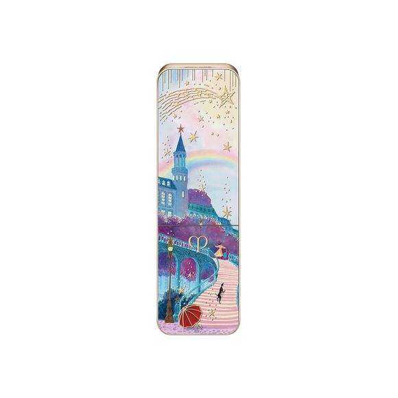 Photo of the 26 AW Holiday Collection limited-edition LIPSTICK case. The closed rectangular gold tube features a scenic illustration of a cobblestone path toward a castle with a rainbow, detailed with figures, a black dog, and a red umbrella.